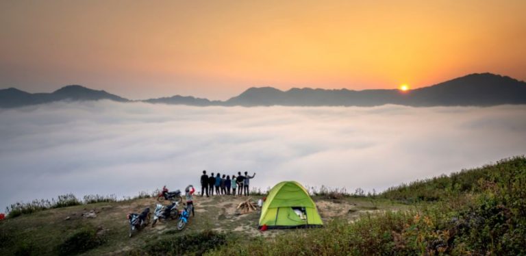 People standing at a camping site, looking out over the clouds.
