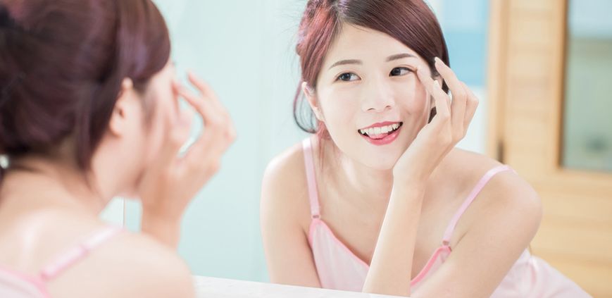 A woman looking at her eyelashes in the mirror.
