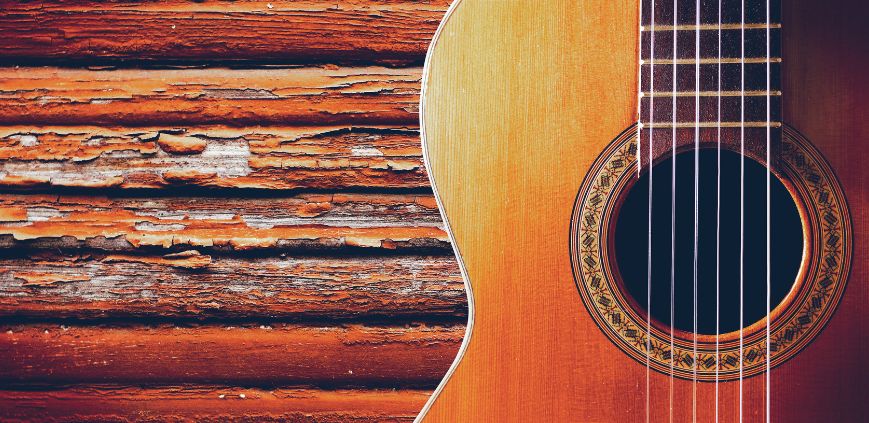 A close up of an acoustic guitar leaning up against a wooden panel wall