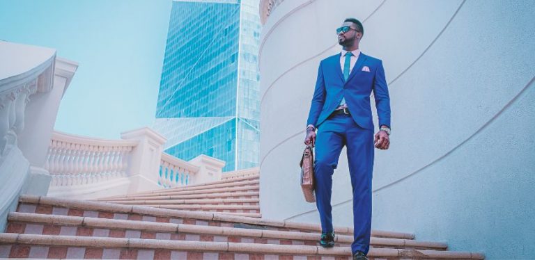 A man in a tailored blue suit, walking down a set of stairs on an outdoor building.