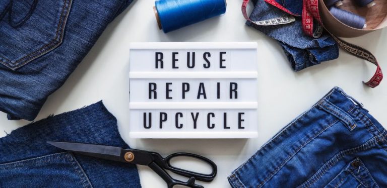 Pairs of blue jeans with scissors on a table with a sign that says "reuse, repair, upcycle"