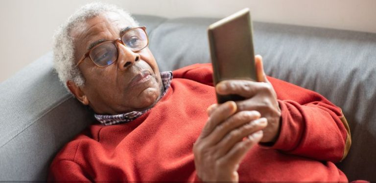 An older man laying on a couch holding a cell phone.