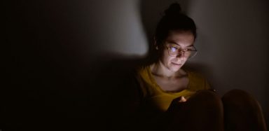 A woman sitting in the dark by herself, using her cell phone