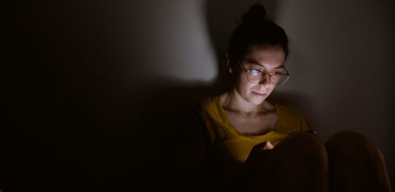 A woman sitting in the dark by herself, using her cell phone